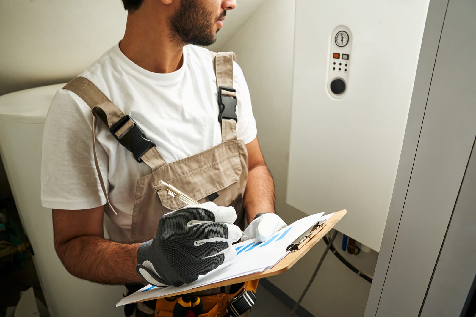 service-04 61778964-professional-male-handyman-in-uniform-is-checking-gas-boiler-at-home-and-making-notes-in-tablet